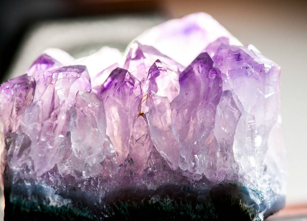 A hand holding raw amethyst and rose quartz on a linen cloth, what are crystals used for spiritually